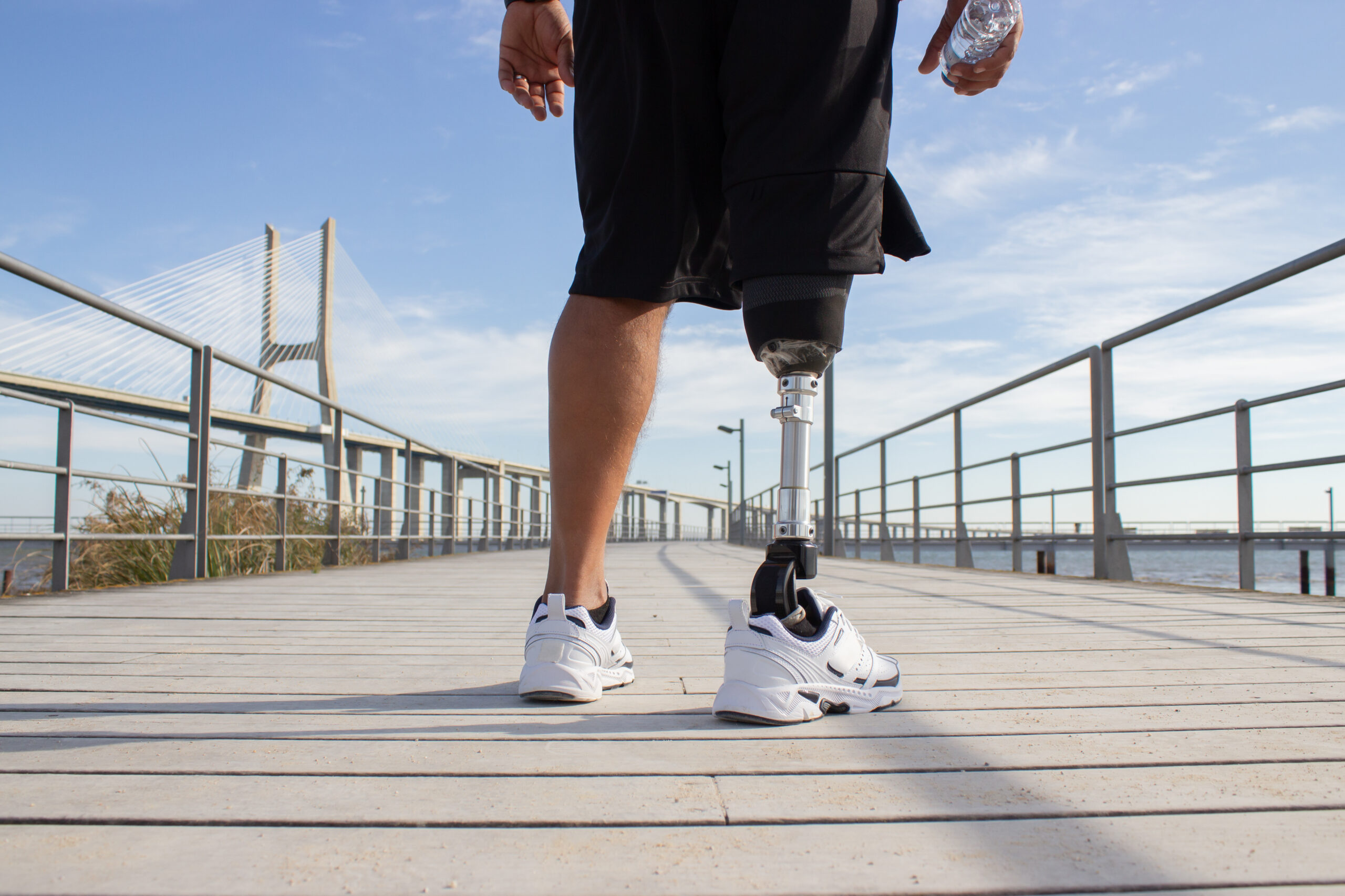 Back view of man with mechanical leg on sunny day. Sportsman in black shorts and white sneakers photographed during training. Sport, disability, hobby concept
